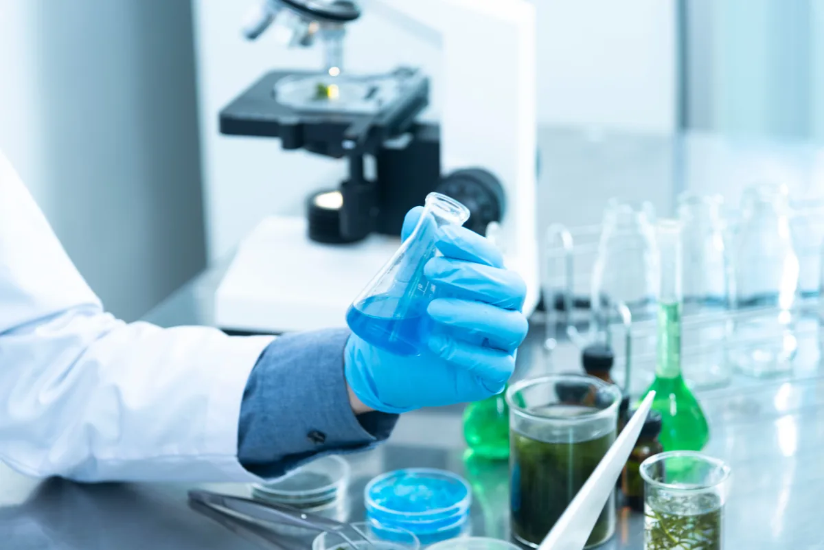 Gloved scientist holding a flask in a laboratory.